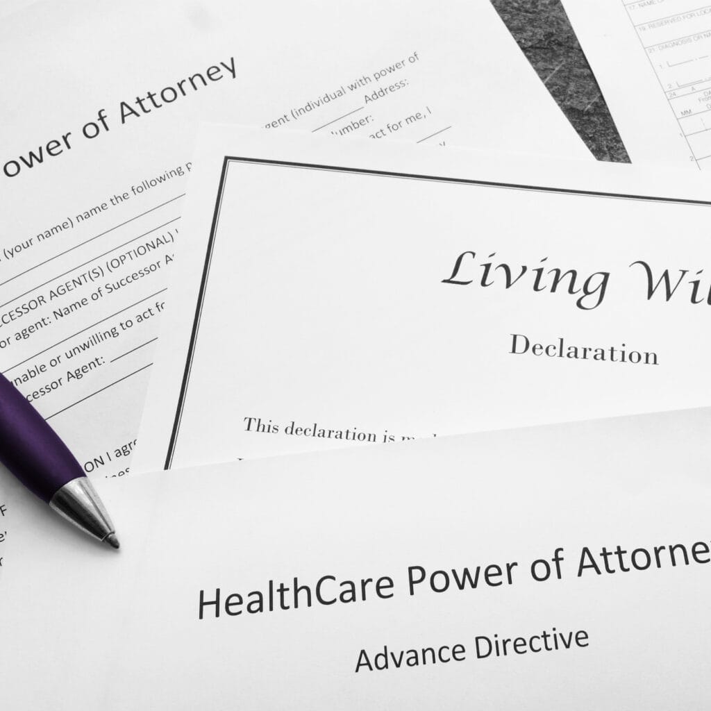 A variety of legal paperwork sits on a table with a pen at the ready, with titles like "Living Will" and "Power of Attorney"