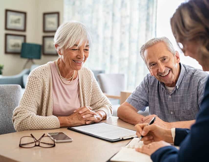 A smiling older couple sits across from an official looking person with a paper and pen, they all appear to be in conversation