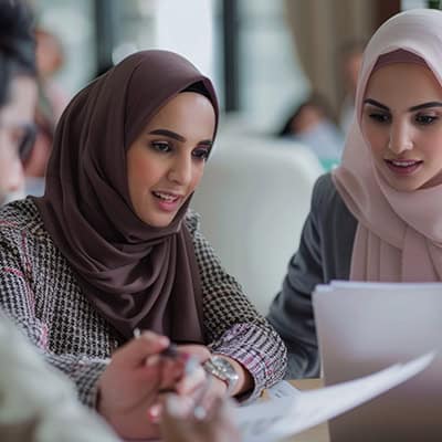 2 young women in hijabs are looking over important paperwork with a professional looking person