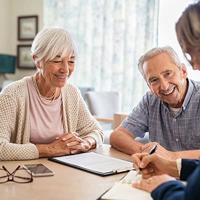 A smiling older couple sits across from an official looking person with a paper and pen, they all appear to be in conversation