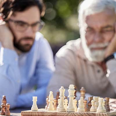 A father and son look deep in thought at the chessboard in front of them, considering their next move