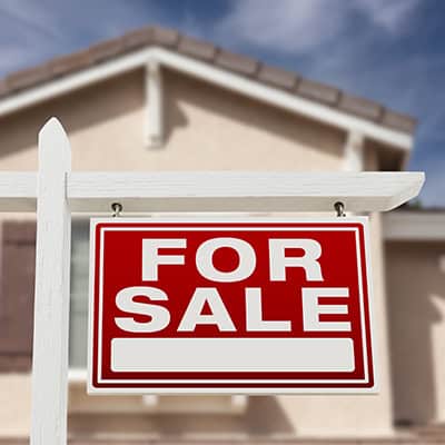 A large "FOR SALE" sign is in front of a house