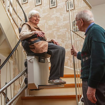 A woman operates her stair assist lift, as her husband watches from the foot of the stairs