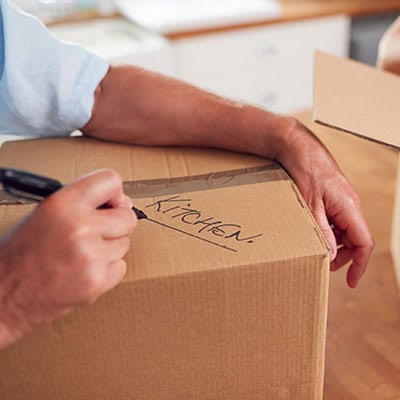 Close up of a hand with a marker writing "kitchen" on a moving box