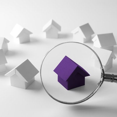 A circle of small white wooden houses, one is purple and enhanced under a magnifying glass, as if being inspected