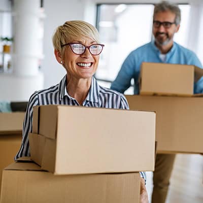 A smiling man and a woman carry moving boxes