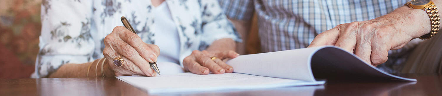Close up of a senior citizen's hand signing important looking legal paperwork with a pen.