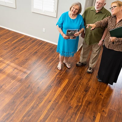 Shot from above, 3 people are standing in the doorway of an empty room with hardwood floors, admiring the space