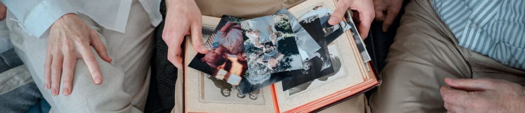 Shot from above, a closeup of a family photo album spread across the laps of 3 people