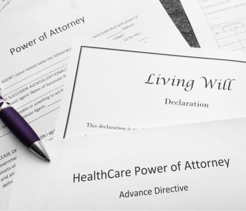 A variety of legal paperwork sits on a table with a pen at the ready, with titles like "Living Will" and "Power of Attorney"